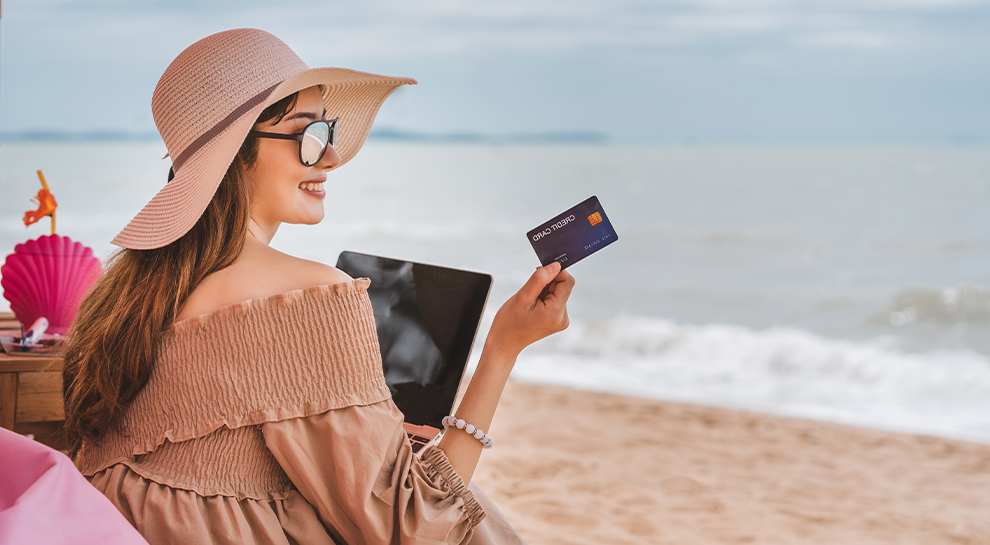 kobieta siedzącą na plaży trzymająca w ręku kartę kredytową